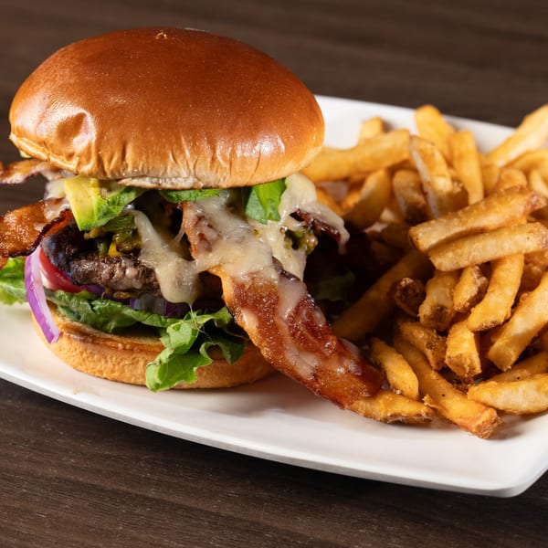 A Tukee's Sports Grille bacon avocado burger with melted cheese and fries on a white plate.