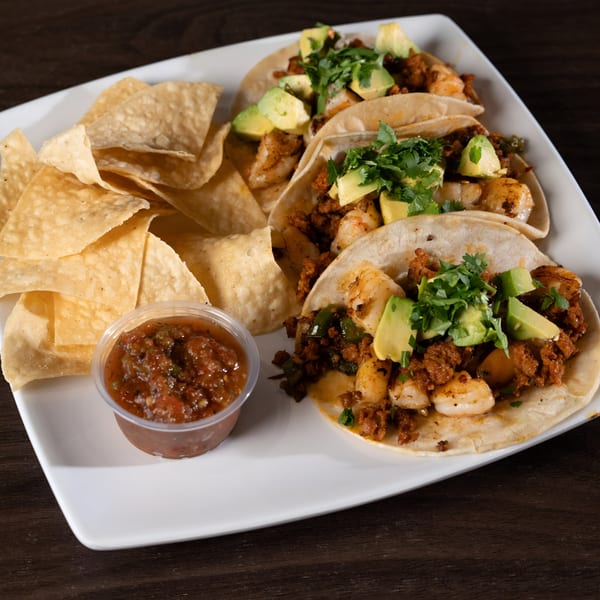Three shrimp and chorizo tacos with avocado and cilantro, served with tortilla chips and salsa.
