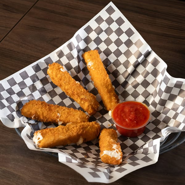 Golden-brown mozzarella sticks with melted cheese and a side of red marinara sauce in a basket.
