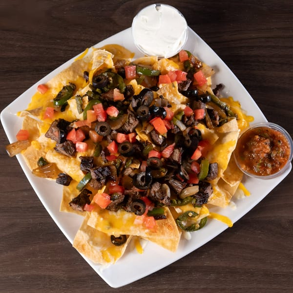 A plate of Tukee's Sports Grille nachos with steak, cheese, olives, tomatoes, and peppers.