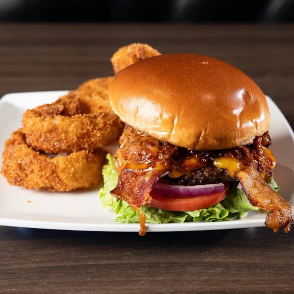 A Tukee's Sports Grille burger with bacon, cheese, lettuce, tomato, onion, and a side of onion rings.